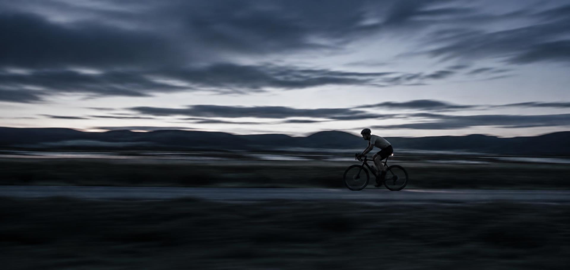 Cyclist crossing an open landscape at dusk